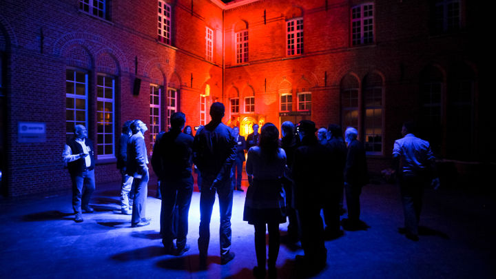 En stor grupp människor samtalar utanför en snyggt upplyst byggnad i Turnhout, Belgien, vid en workshop som arrangerats av Philips