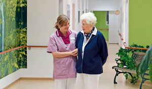 En sköterska tar hand om en äldre patient i en upplyst hall