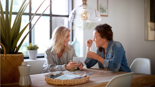 Två kvinnor hemma som har en konversation under en Philips-glödlampa
