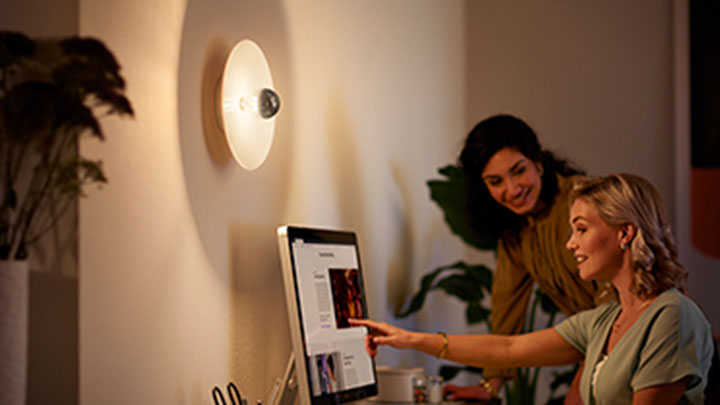 Kvinna arbetar på sin dator brevid en väggmonterad LED mirror glödlampa