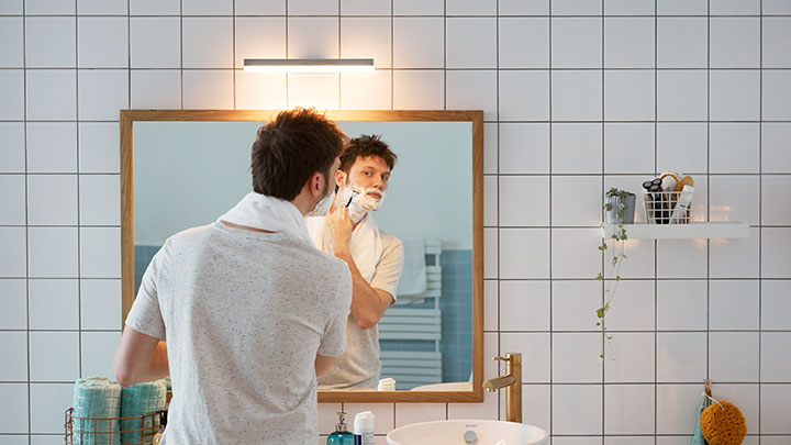 En man rakar sig framför badrums spegeln belyst av en väggmonterad Philips LED