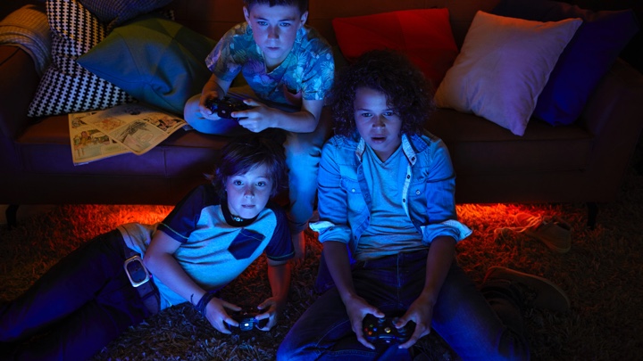 3 pojkar som spelar videospel med stämningsbelysning	